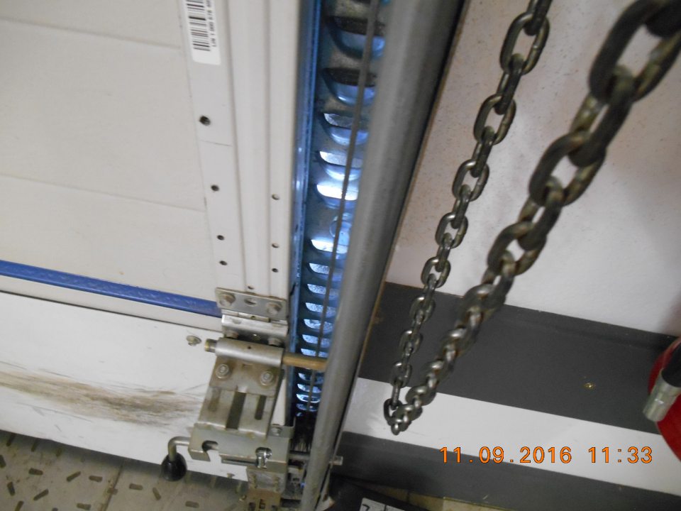 Poškodené ukotvenie rámu rolovacej brány na rampe príjmu tovaru.