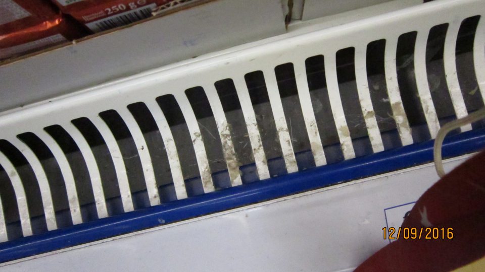 Znečistená mriežka a priestor pod mriežkou chladiacej vitríny  na predajnej ploche