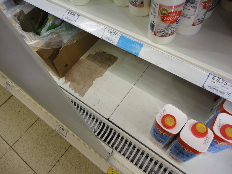 Na predajnej ploche regál chladiaceho zariadenia na mliečne výrobky je znečistený nánsmi prachu, prilepeným kartónovým obalom. 