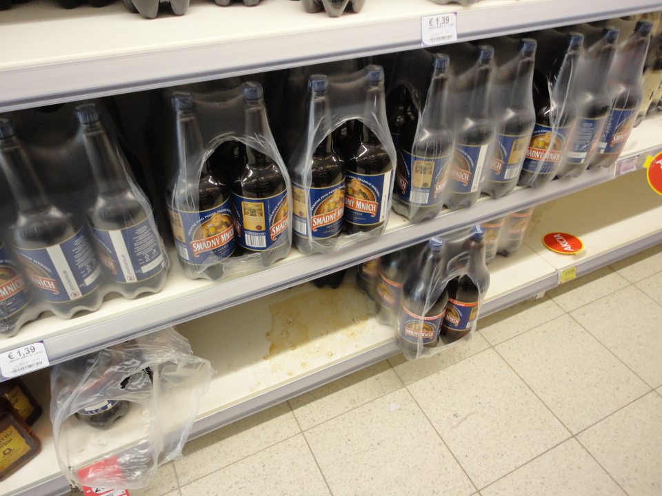 Na predajnej ploche regál s uloženým pivom znečistený zaschnutými škvrnami po vytečenej tekutine. 