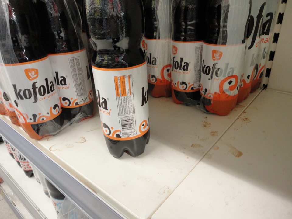 Na predajnej ploche regál s uloženými nealkoholickými nápojmi (kofola) znečistený zaschnutými škvrnami po vytečenej tekutine. 