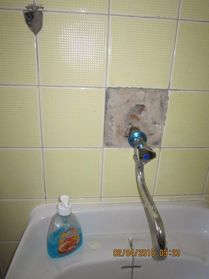 Poškodená stena pri umývadle na prevádzke.
