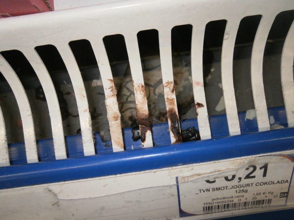 Znečistená mriežka a priestor pod mriežkou v chladiacej vitríne s jogurtami na predajnej ploche