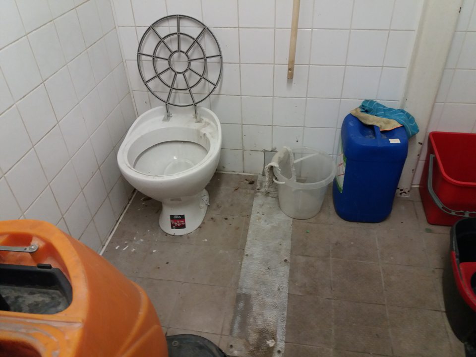 Znečistená podlaha, obklad steny a výlevka v miestnosti s čistiacim strojom.