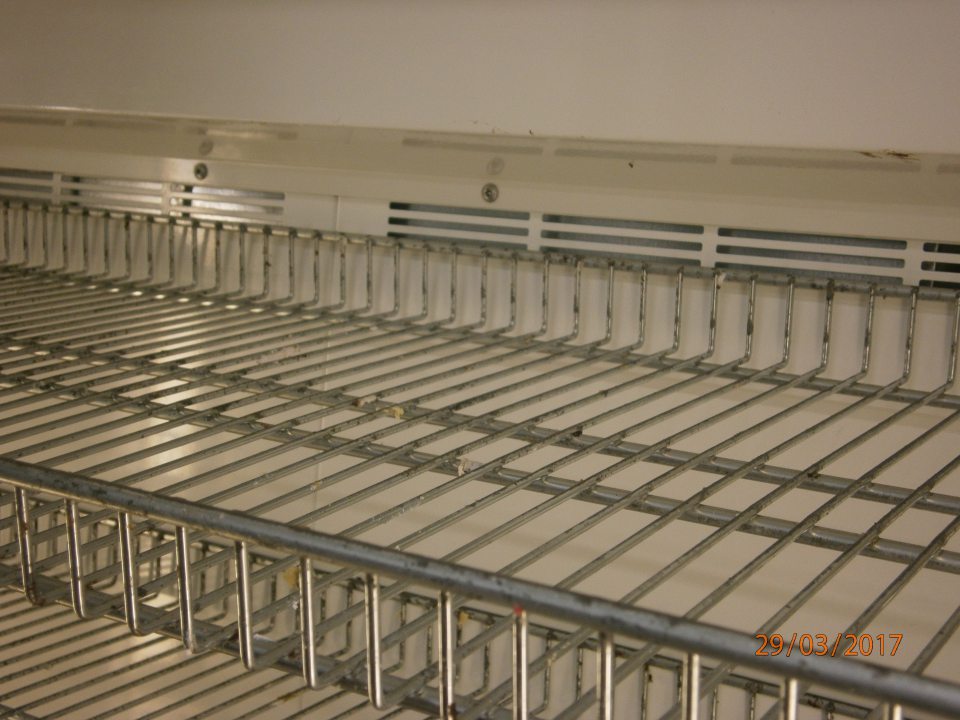 Znečistený vnútorný priestor a police príručnej chladničky na zákusky v sklade chleba a pečiva.