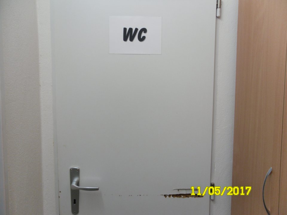 Poškodené dvere pri vstupe do sociálneho zariadenia.