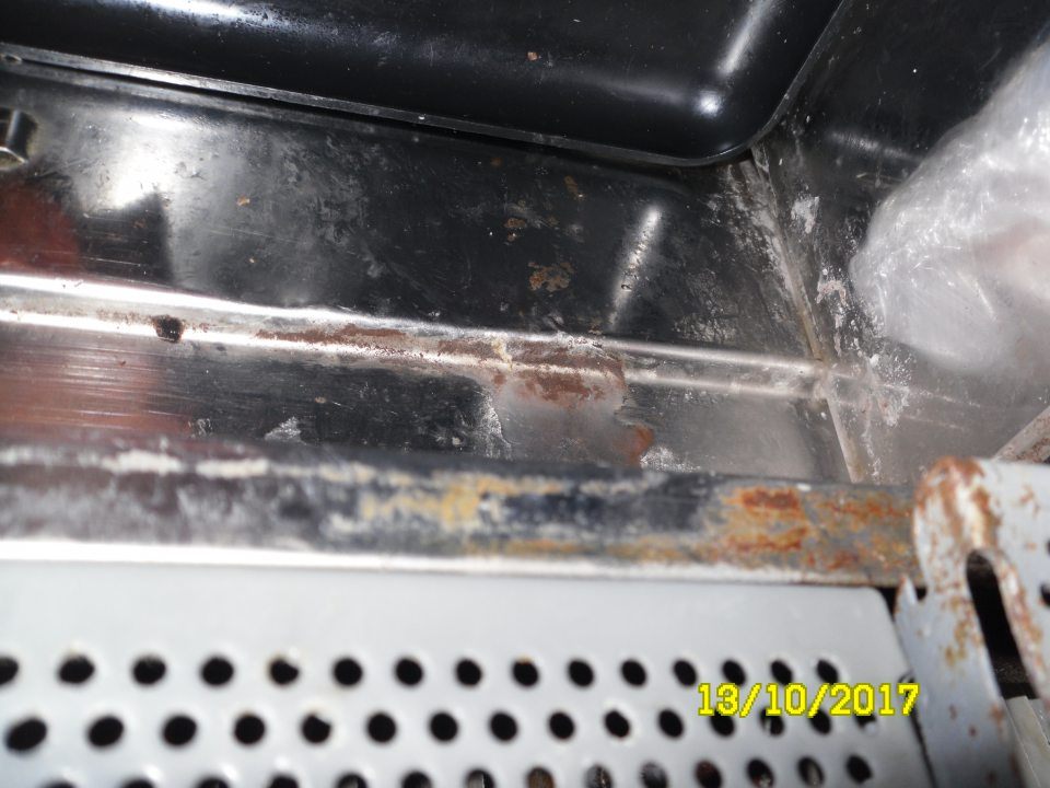 Znečistená a miestami korodujúca zadná stena chladiarenskej vitríny s uchovávanými mäsovými výrobkami.