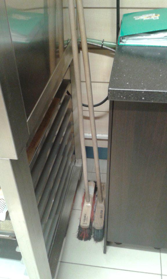 V priestore dopekania pekárskych výrobkov vedľa regálu s plechmi uložené metly. 