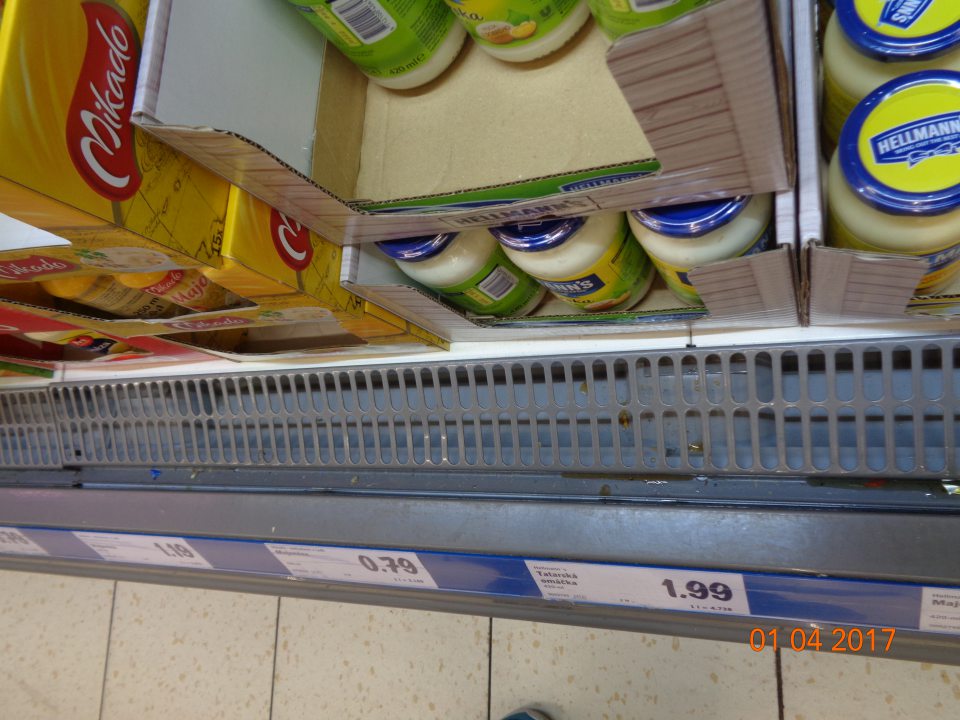 Znečistené mriežky/priestor pod mriežkami chladiacich zariadení na predajnej ploche prachom, obalovým materiálom, vytečeným zaschnutým obsahom neidentifikovateľných potravín a drobnými nečistotami.