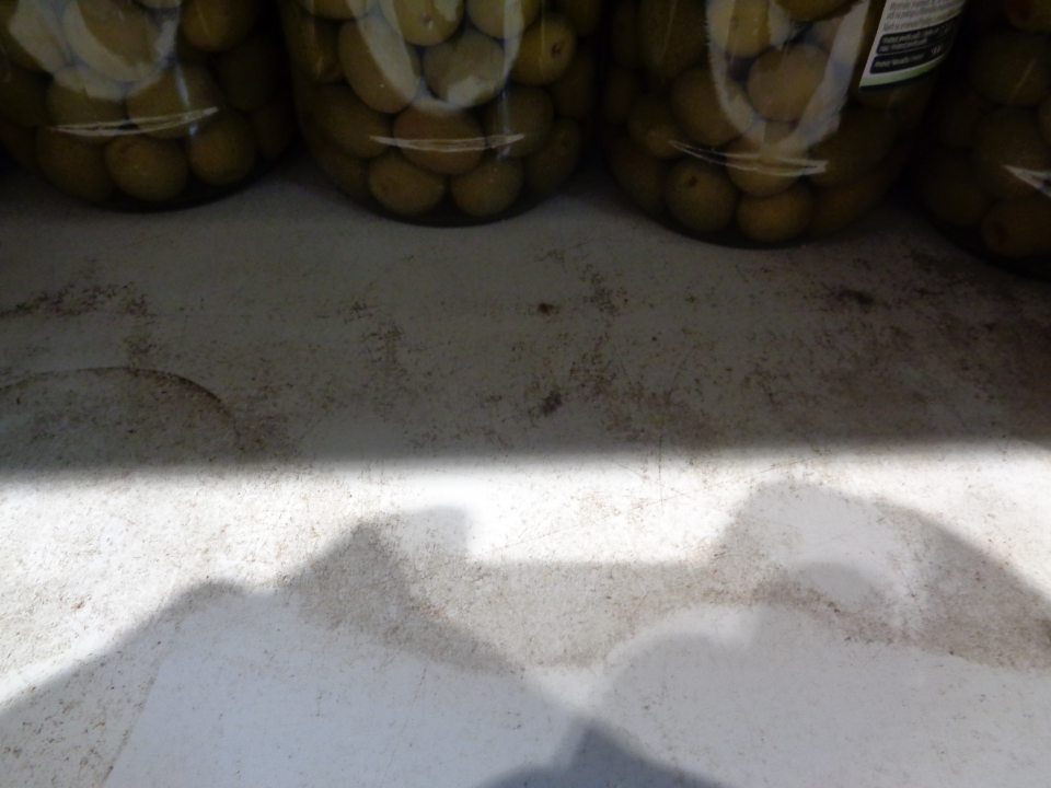 V predajni polica v regáli znečistená prachom a zaschnutými škvrnami po vytečenej tekutine.