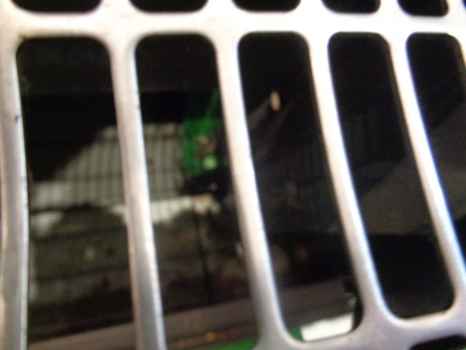 Priestor pod mriežkou v chladiacom zariadení s kvasenou kapustou a šampiňónmi znečistený prachom, zastaranou špinou, zvyškami uložených potravín a zaschnutými škvrnami po vytečenej tekutine.