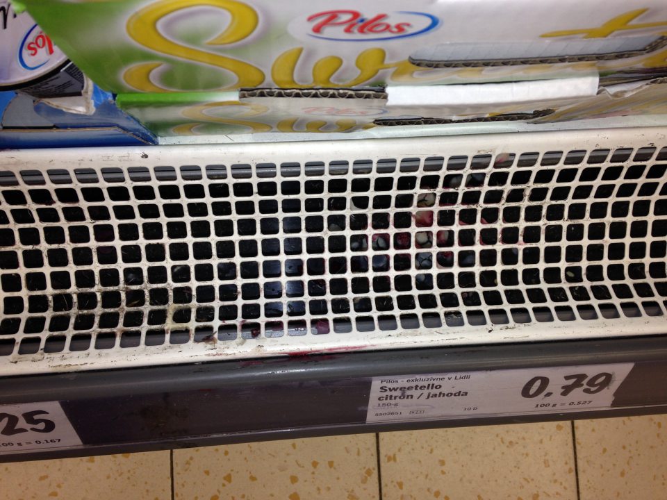 V predajni znečistená ochranná mriežka chladiacej vitríny s jogurtami.