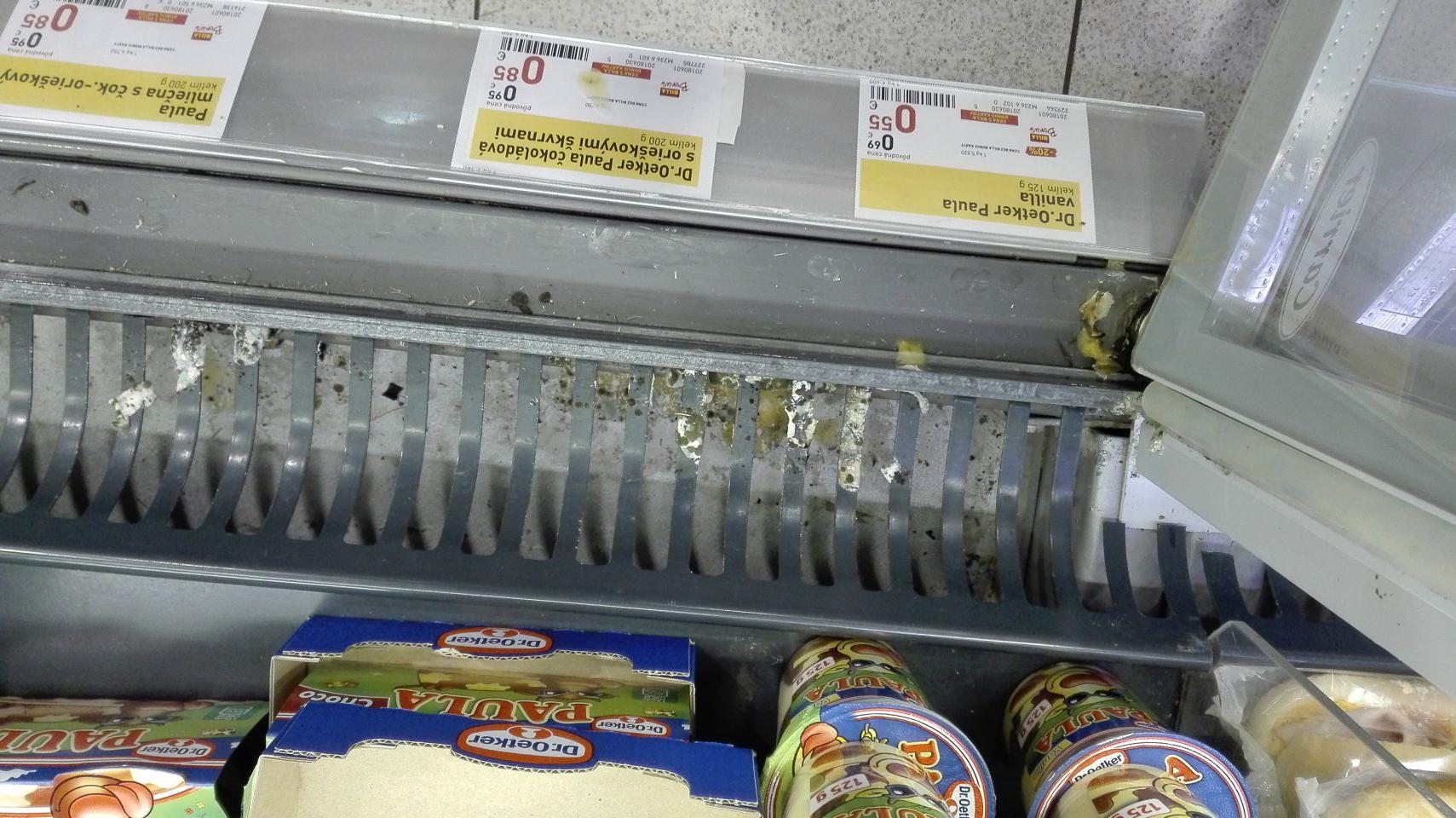 Znečistená mriežka a priestor pod mriežkou v chladiacej vitríne s ponukou mliečnych výrobkov.