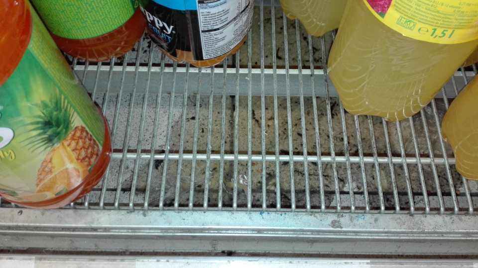 Znečistená podlaha pod regálom s nápojmi na predajnej ploche.