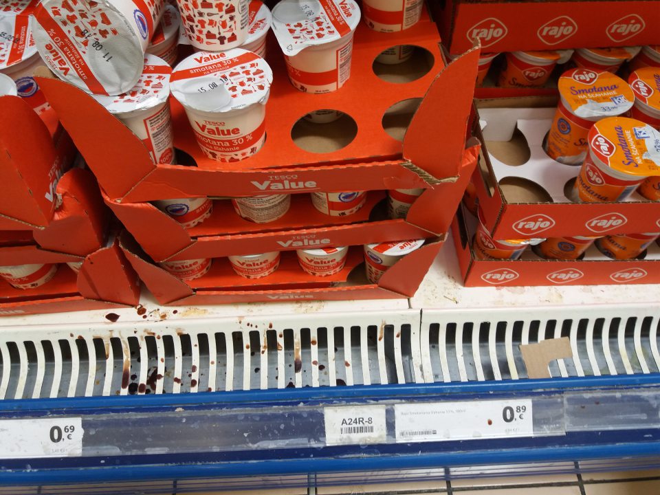 Znečistená spodná polica, mriežka a priestor pod mriežkou chladiacej vitríny s ponukou mliečnych výrobkov.