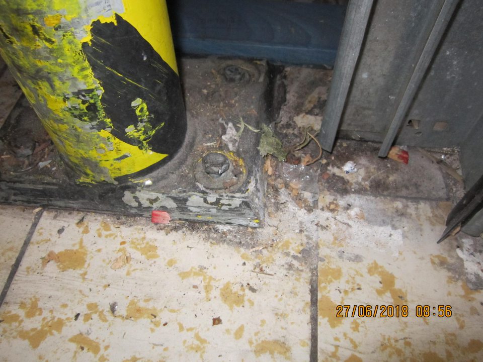 V rohoch pri príjmových dverách znečistená podlaha zaschnutou špinou, kúskami dreva paliet, zhlukmi prachu.