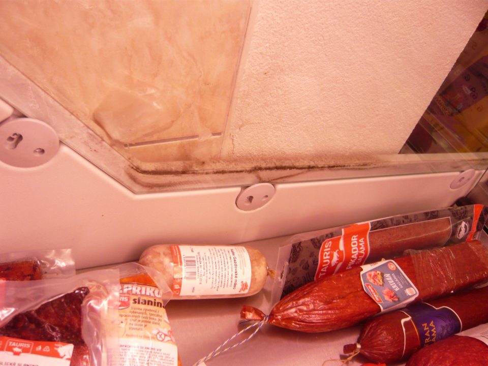 Znečistená chladiarenská vitrína s uchovávanými mäsovými výrobkami na predajnej ploche.