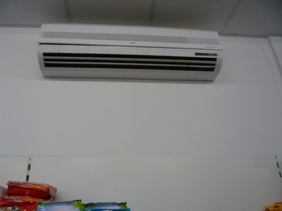 Znečistená klimatizačná jednotka na strope nad regálmi s balenými potravinami.