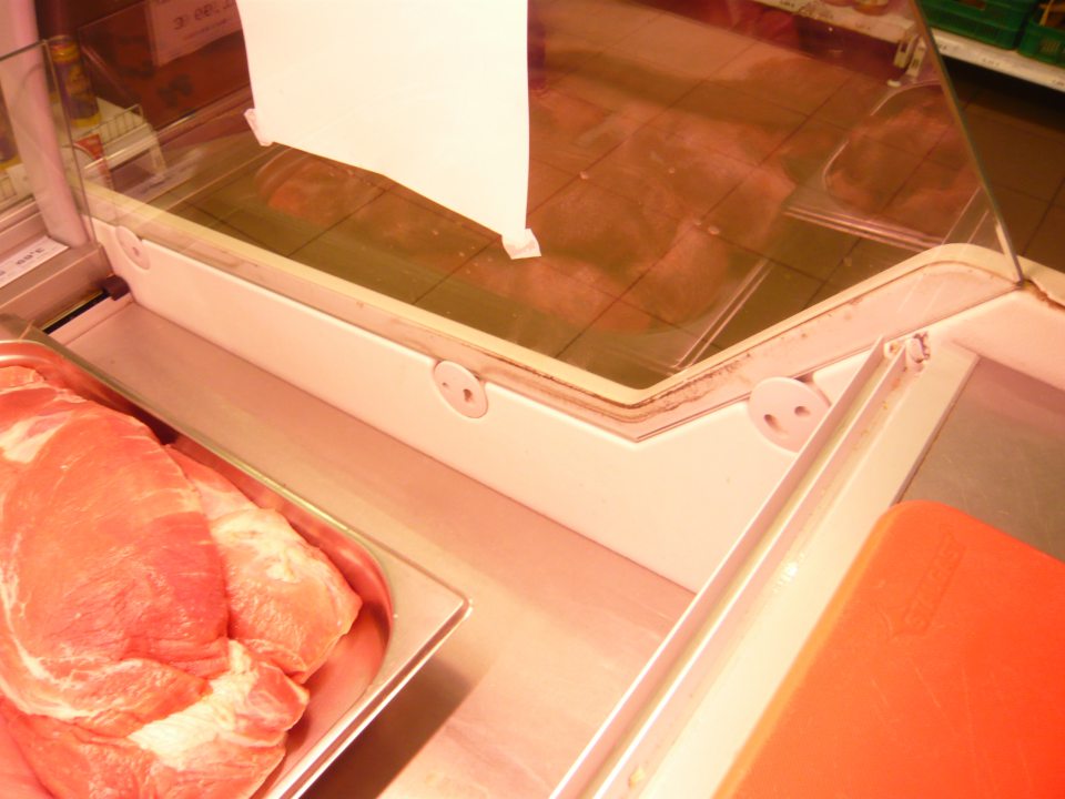 Zistená znečistená vitrína s uchovávanými mäsovými výrobkami na predajnej ploche, a to medzi vonkajšou skanenou stenou a kovovou konštrukciou.