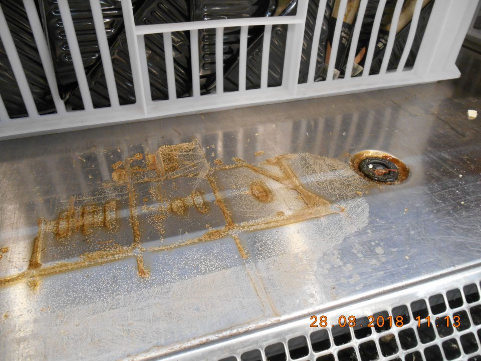 Znečistené dno a priestor pod mriežkou v chladiacej vitríne na predajnej ploche.