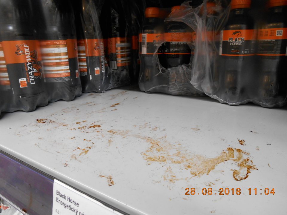 Znečistený regál pod energetickými nápojmi na predajnej ploche.