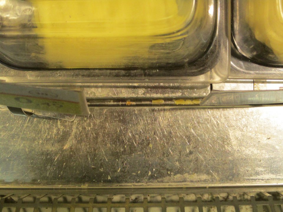 pult chladiarenského obslužného pultu medzi a pod nerezovými platňami znečistený kúskami predávaných potravín (syry)