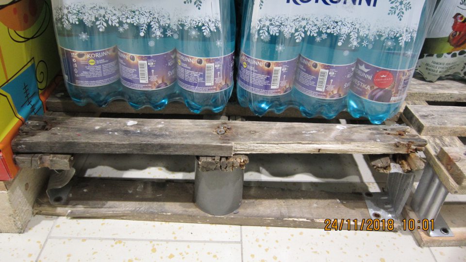 Značne mechanicky poškodené drevené palety, na predajnej ploche, na ktorých sú uchovávané nealko nápoje.
