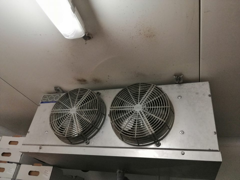 Znečistené a zaprášené mriežky ventilátora chladiacej jednotky a strop v chladenom sklade ovocia a zeleniny.