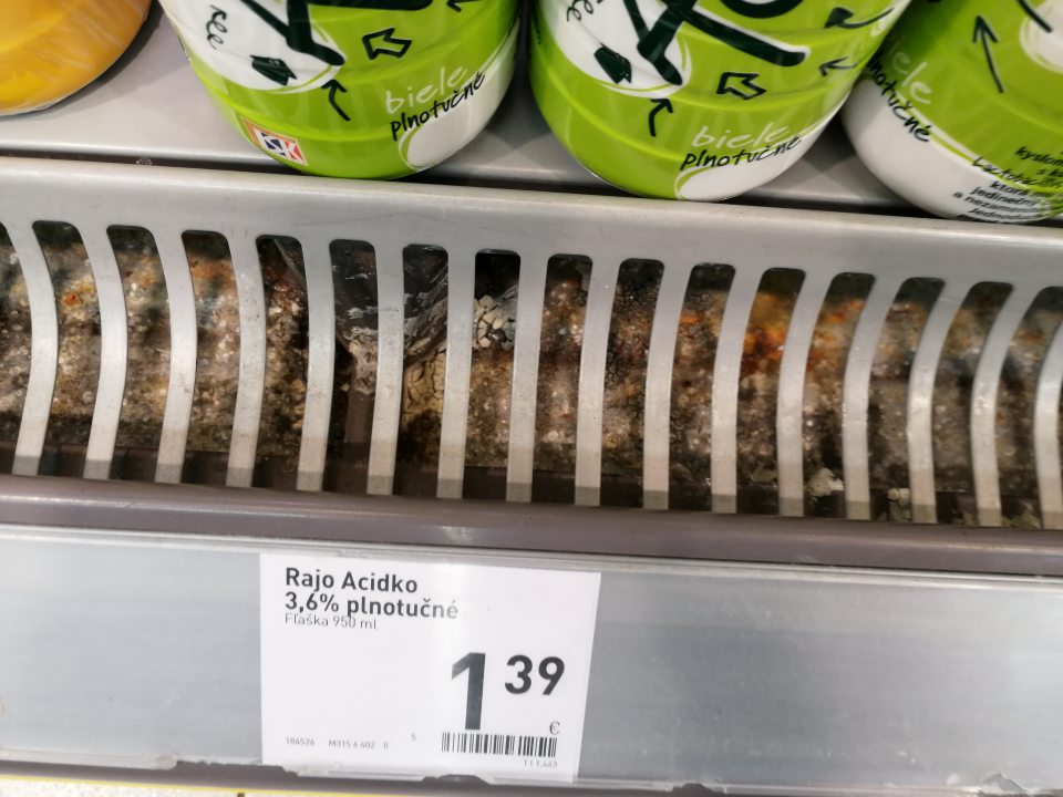 Znečistený priestor pod mriežkou v chladiacej vitríne s ponukou mliečnych výrobkov.