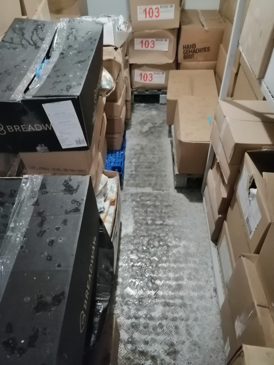 Vrstva ľadu na podlahe a zamrznutý kondenzát na krabiciach s tovarom v mraziacom boxe pekárne.