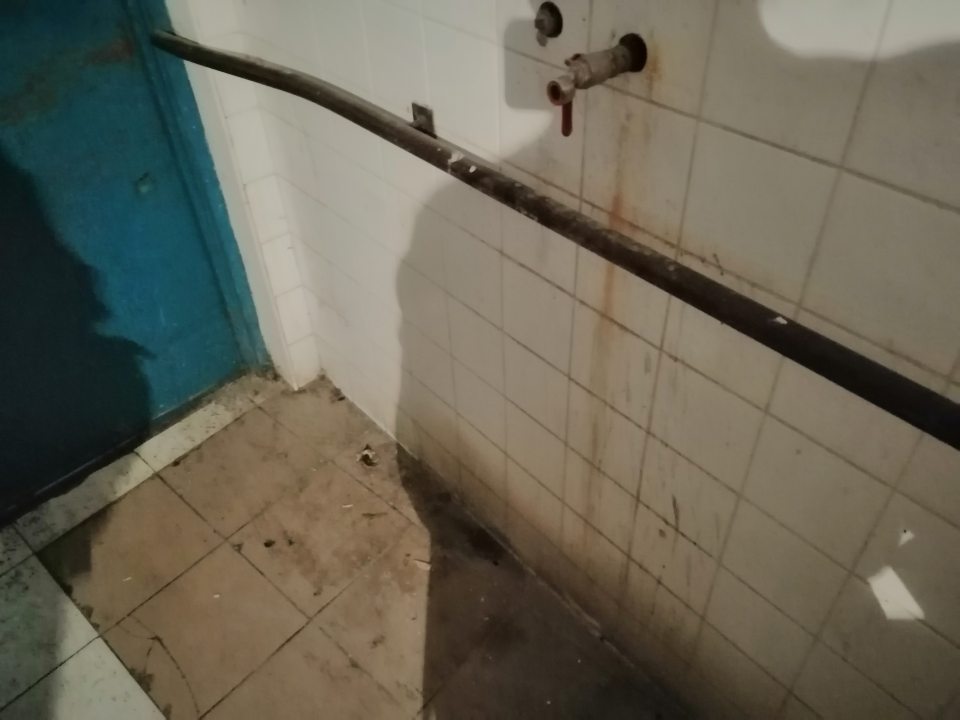 Znečistená podlaha a obklad stien v miestnosti s kontajnermi na odpad.