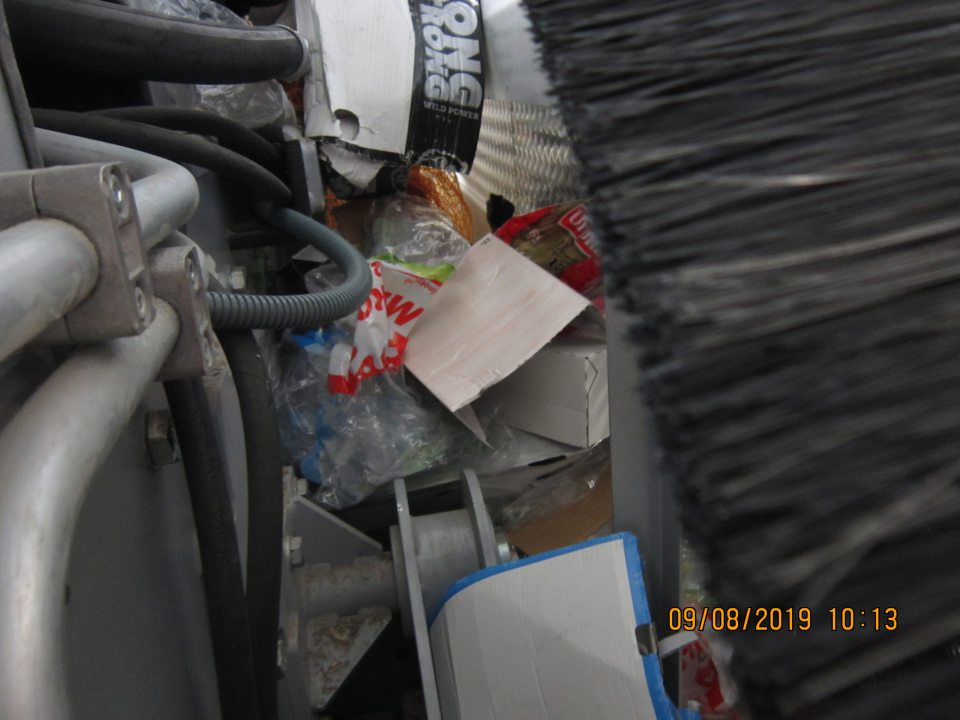 Veľký neporiadok v priestore medzi lisom na kartóny a stenou skladu. Priestor bol zahádzaný popadanými kartónmi a igelitmi vo veľkom množstve