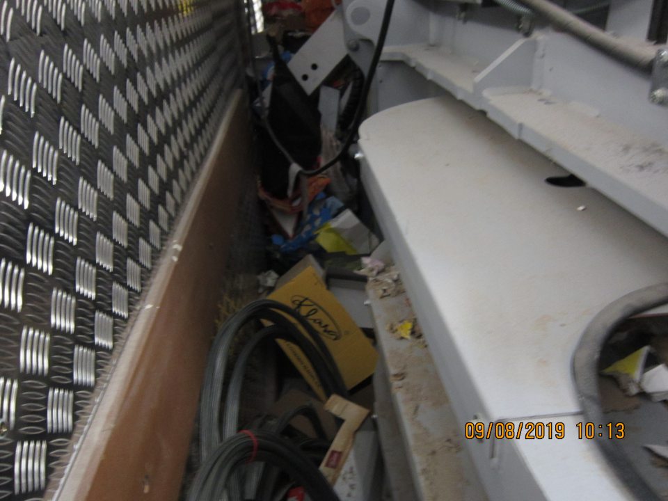 Veľký neporiadok v priestore medzi lisom na kartóny a stenou skladu. Priestor bol zahádzaný popadanými kartónmi a igelitmi vo veľkom množstve