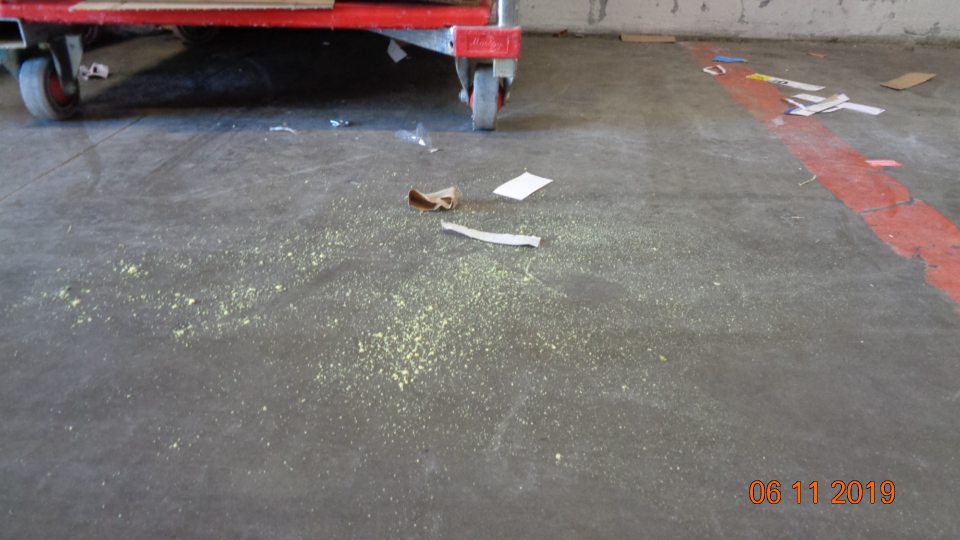 Podlaha v suchom sklade na viacerých miestach znečistená kúskami igelitov, papierov a úlomkov paliet.