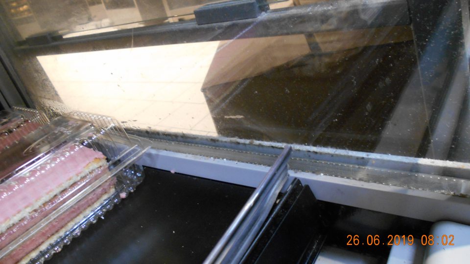 Znečistené chladiarenské zariadenie s uchovávanými cukrárskymi výrobkami, pod mriežkou a medzi sklenými stenami (prach, zvyšky potravín a iné nečistoty).