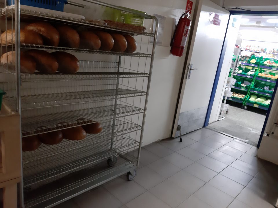 Nehygienické skladovanie nebaleného pečiva - nebalené chleby uložené priamo na kovových policiach regálu, regál umiestnený v manipulačnej chodbe v blízkosti vstupu na predajňu.
