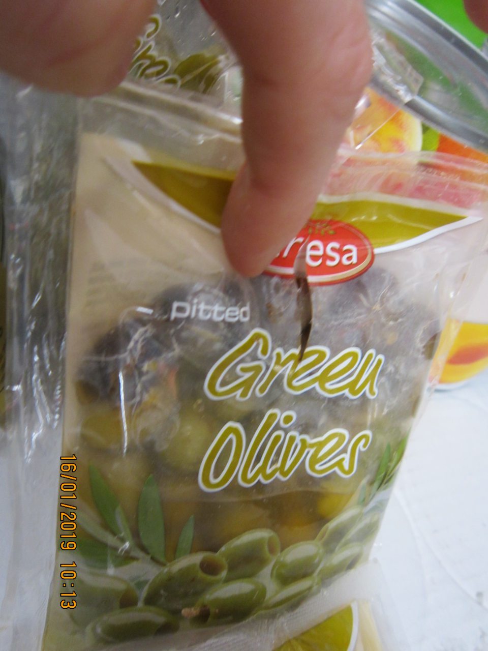 Originálne balenie výrobku s viditeľným poškodením plastového obalu s chýbajúcim vytečeným nálevom  a následným zmeneným sfarbením zelených olív.