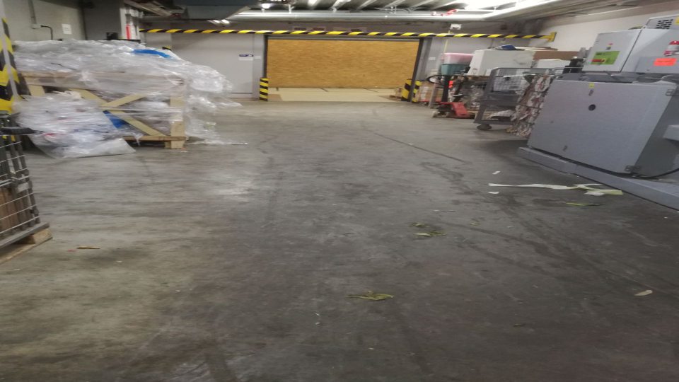 Znečistená podlaha v priestoroch, kde je umiestnený lis na kartónový obal a papier.