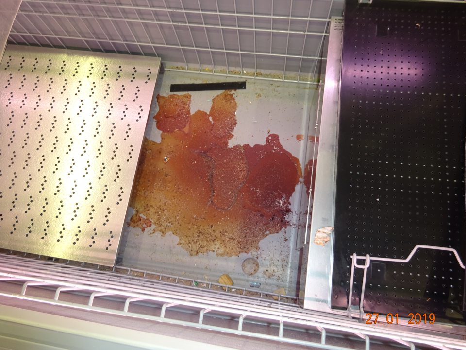 Predajná plocha: znečistenie chladiaceho zariadenia na chladené kurčatá v spodnej časti pod mriežkami zaschnutou potečenou šťavou z mäsa.