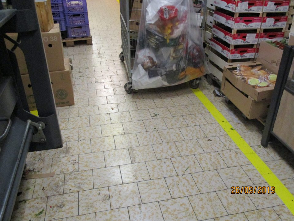 V skladových priestoroch pri zariadení na lisovanie kartónov znešistená podlaha zvyškami potravín, obalového materiálu, drobnými nečistotami, nalepeným prachom.