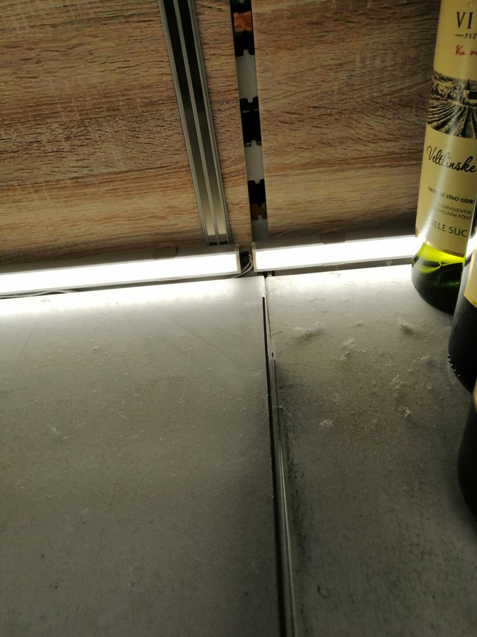 Znečistenie regálu s uloženými alkoholickými nápojmi chuchvalcami prachu.