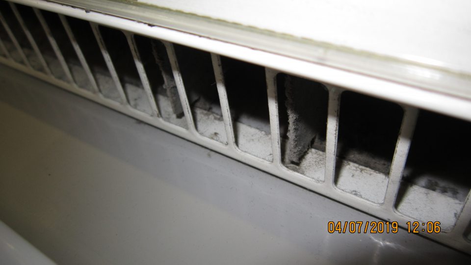 Znečistenie mriežky v spodnej časti chladiacej vitríny nánosom prachu a nečistôt.