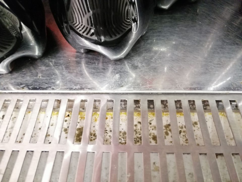 Znečistený priestor pod mriežkou s výskytom plesne v chladiacej vitríne s nealko nápojmi.