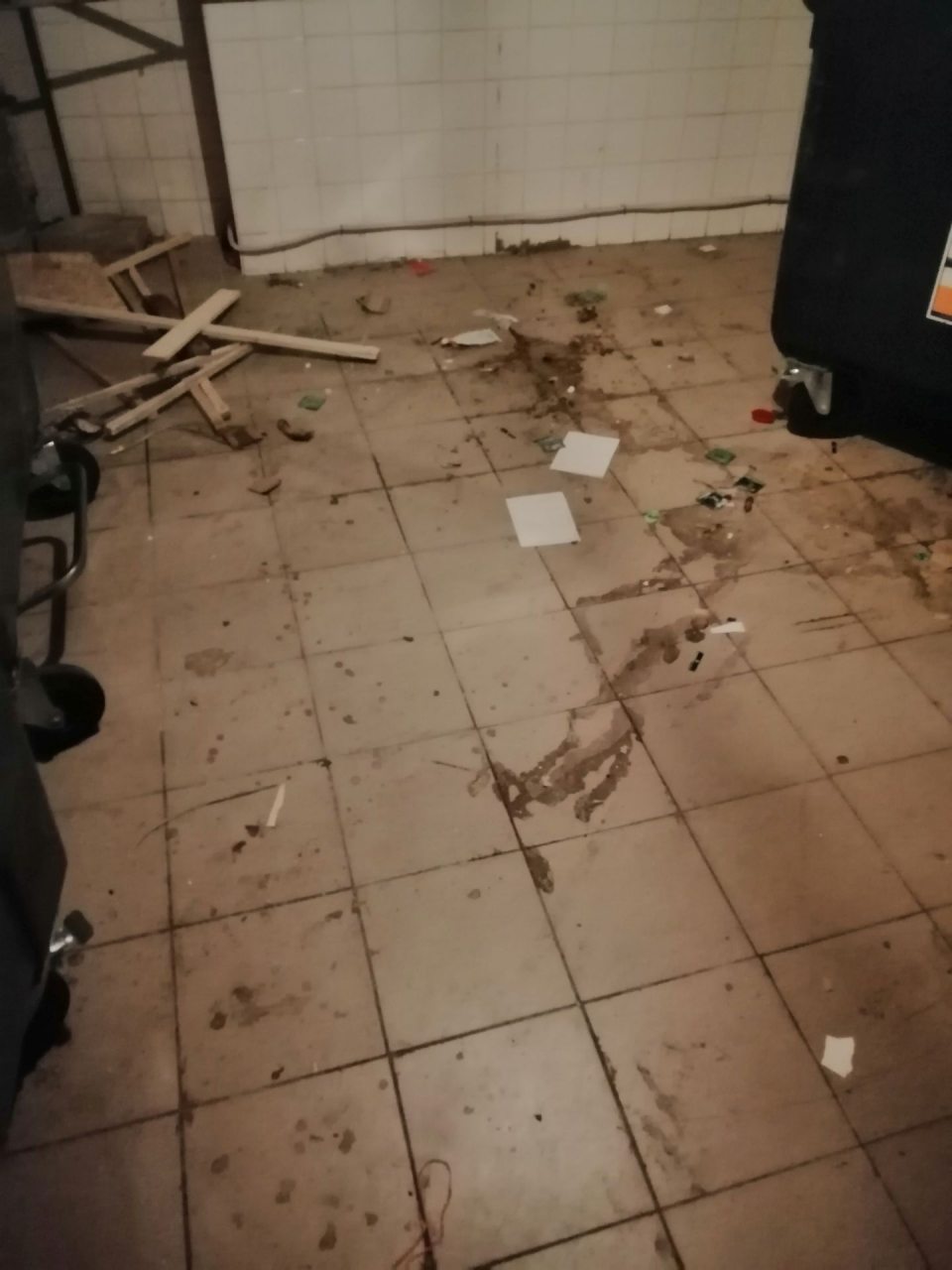 Výrazne znečistená a zatečená podlaha s nánosmi nečistôt, odpadky a zápach v miestnosti s kontajnermi.