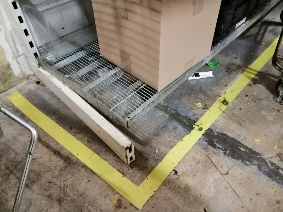 Poškodený regál a znečistená podlaha.