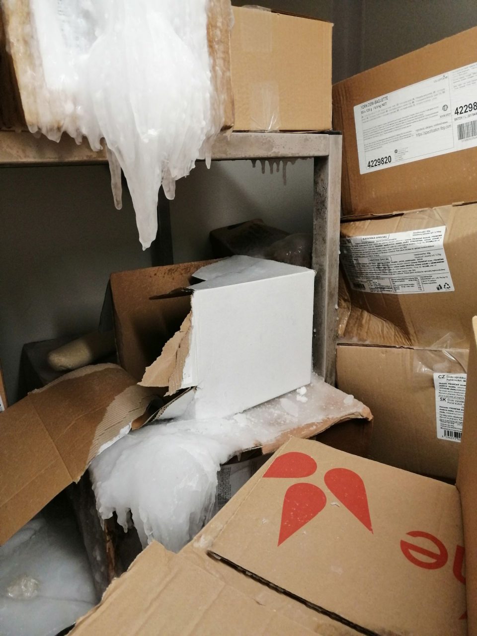 Vrstva ľadu na regáloch a krabiciach s tovarom.