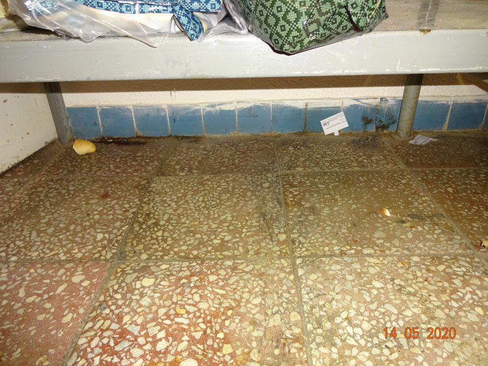 V sklade potravín pod regálmi rôzne zbytky potravín, papierikov, podlaha znečistená, potečená.