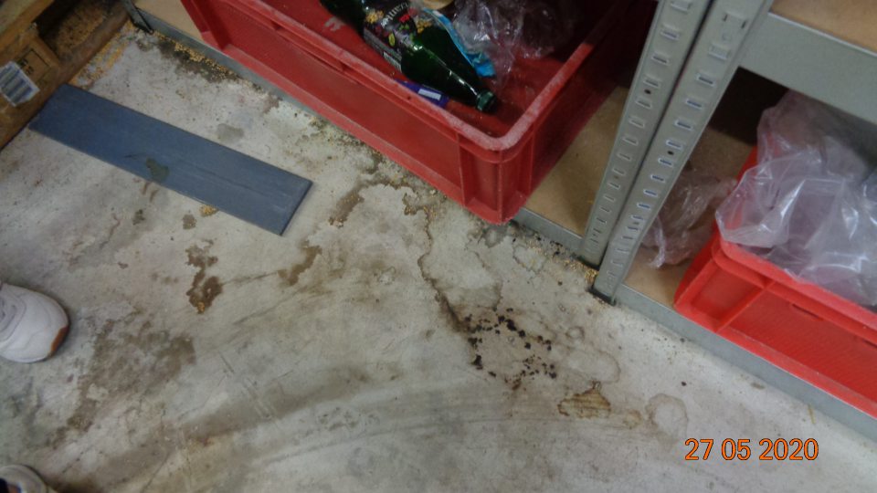 Podlaha v sklade na viacerých miestach znečistená prachom, zvyškami obalov, kartónov, potravín a omrvinkami.