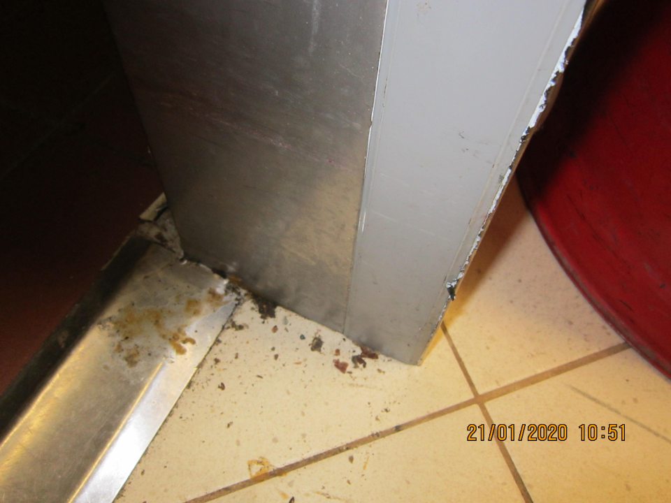 Oddelenie obslužného pultu - nadmerne znečistená podlaha v okolí dverí vstavaného chladiarenského zariadenia od zaschnutej čiernej špiny