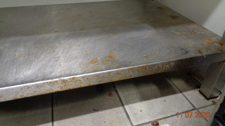 V chladiacom boxe ovocia a zeleniny podlaha pod regálmi znečistená zvyškami potravín, obalov a prachom a skorodované regále.